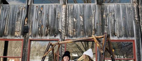A rustic wooden building with large windows and a swing set in front.