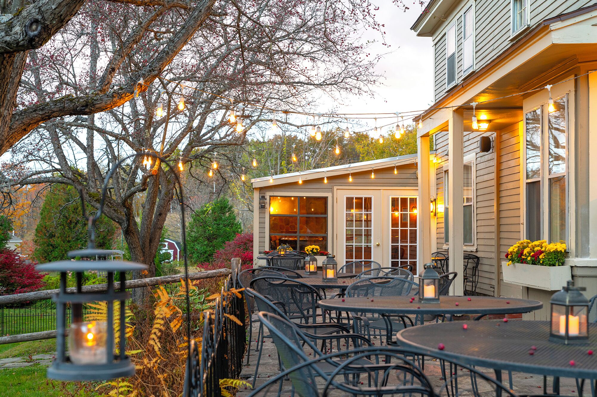 An outdoor patio with tables and chairs, string lights, and lanterns.