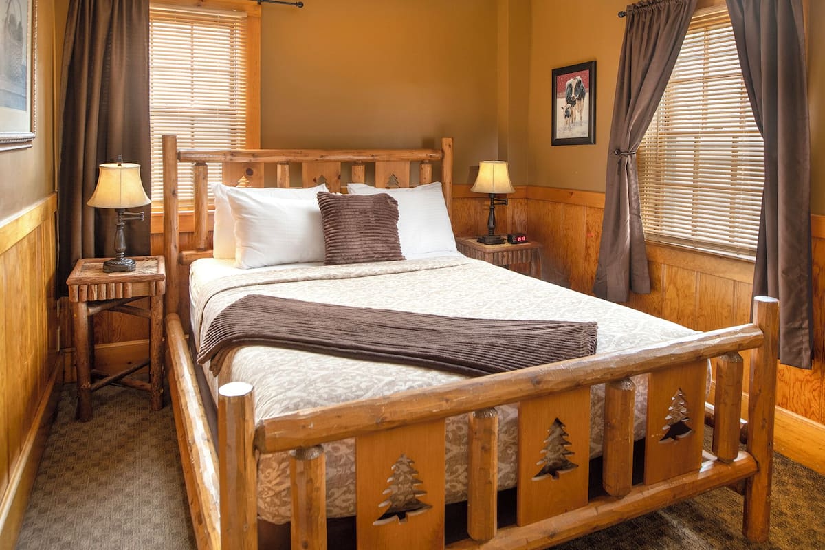 A wooden bed with a headboard, two bedside tables with lamps, and a window with blinds.