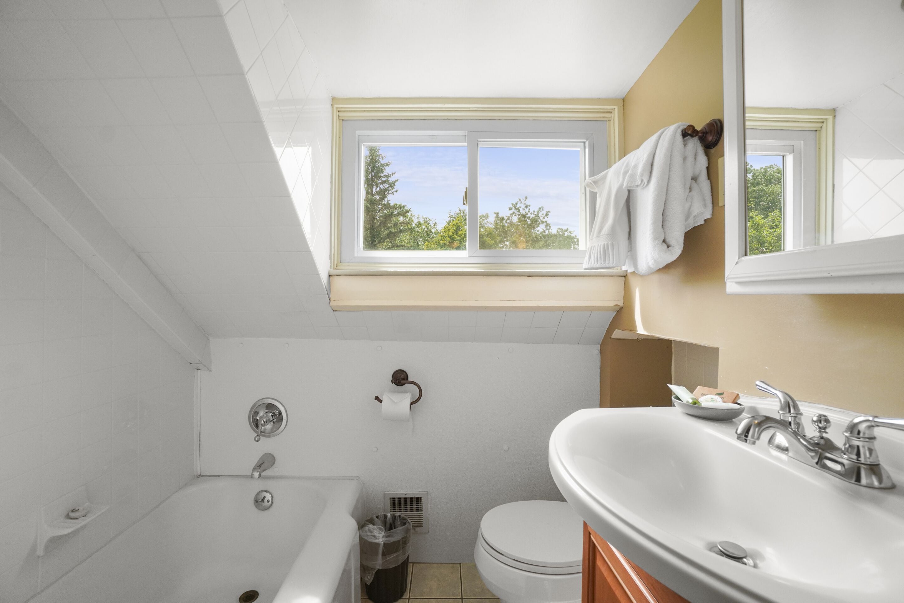 Een badkamer met een bad, toilet, wastafel en een raam met een handdoek aan de muur.