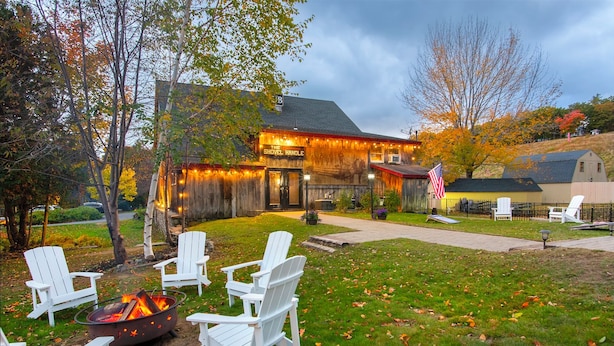 A rustic wooden building with a sign reading "The Travel Handle." There are white Adirondack chairs arranged around a fire pit. - Whitneys Inn at Black Mountain (Jackson)