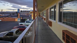 A hotel corridor with large windows, a parking lot with several cars, and a view of a distant landscape. - Best Motel (Barstow)