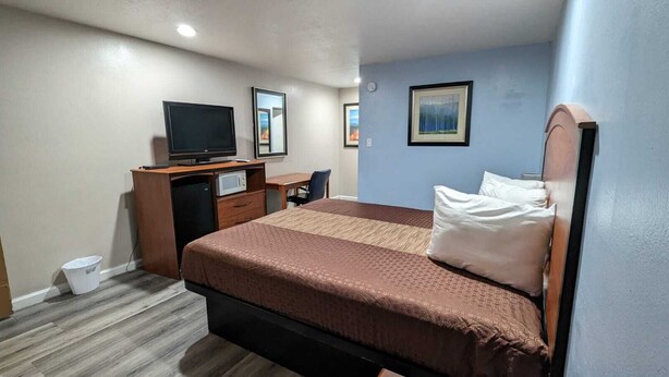 A hotel room with a bed, a desk with a computer, a TV, and a small trash bin. - Best Motel (Barstow)