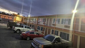A parking lot with several vehicles, including a white pickup truck and a red sedan, in front of a building with multiple balconies and large windows. - Best Motel (Barstow)