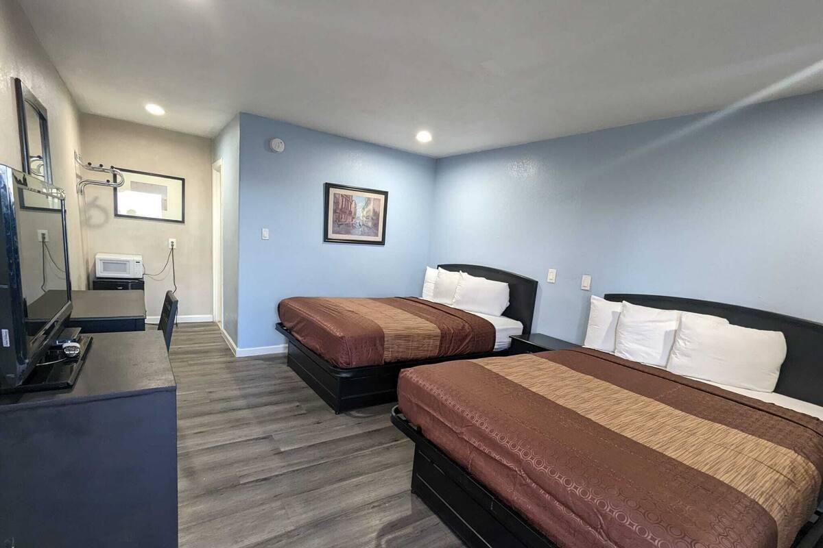 A hotel room with two beds, a TV, a microwave, and a picture on the wall.