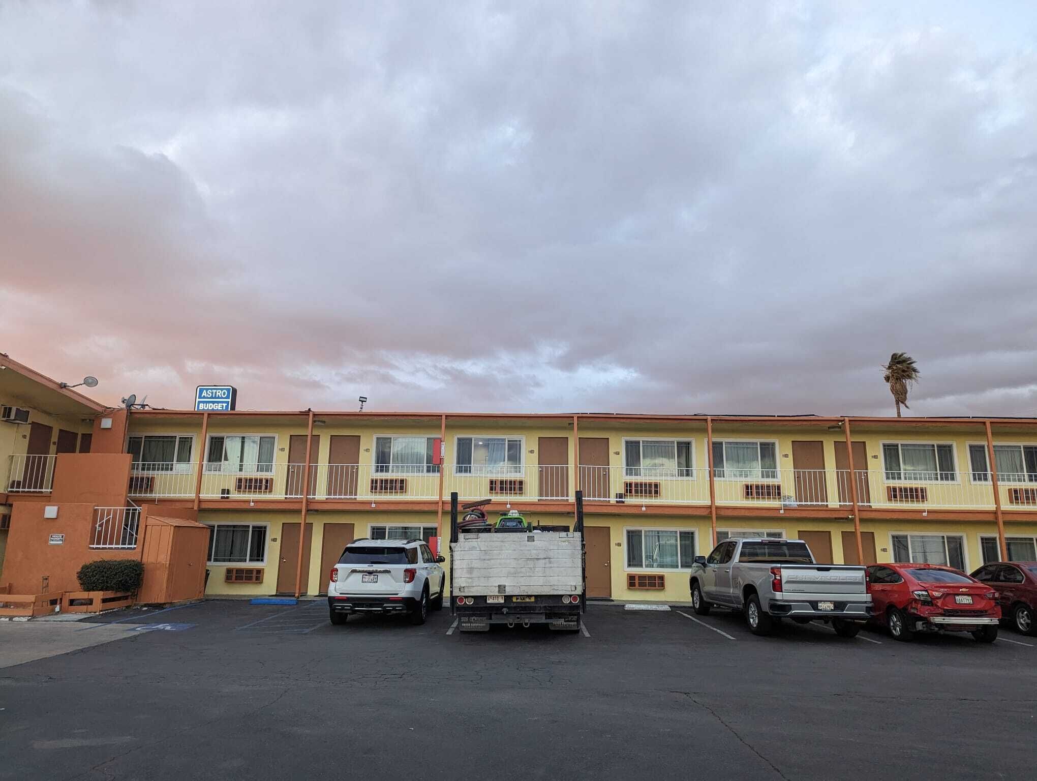 A motel with a parking lot, a white truck, and several cars parked in front.