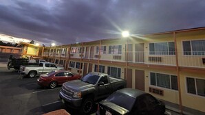 A parking lot with several vehicles, a building with multiple floors and balconies, and a streetlight. - Best Motel (Barstow)