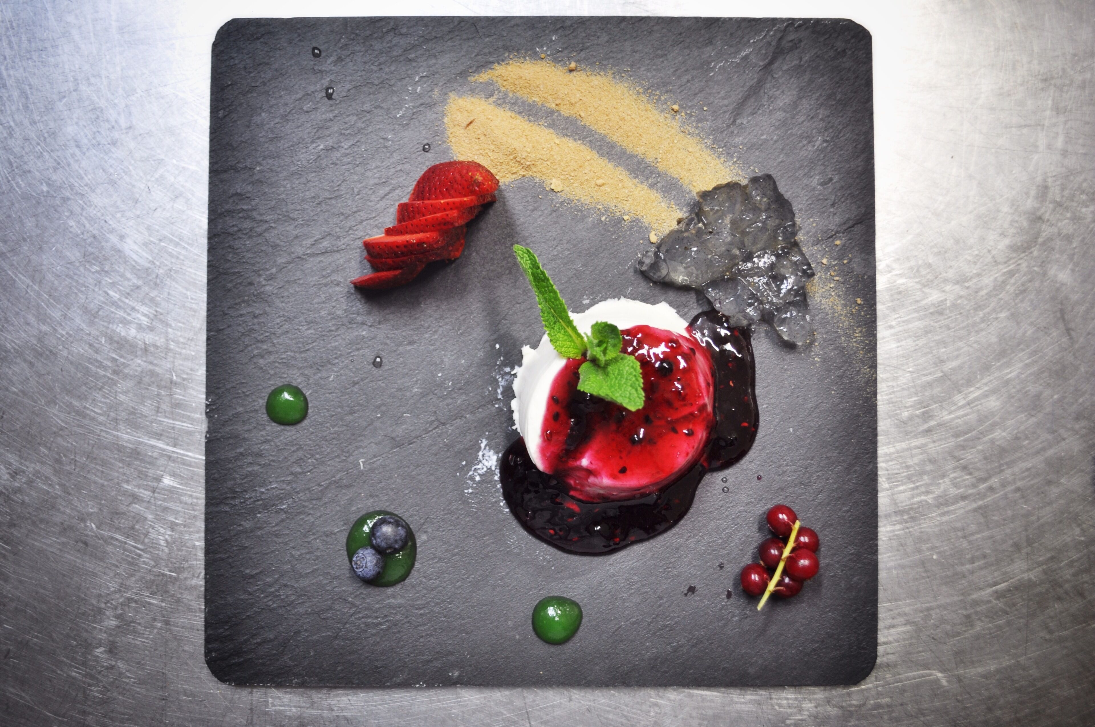 Un dessert servi sur une assiette en ardoise, garni de baies et d’une feuille de menthe.
