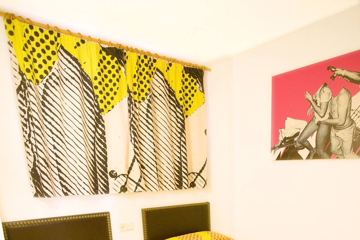 Una habitación con dos camas, cada una con una colcha estampada. Hay una obra de arte en la pared sobre las camas y un cuadro enmarcado a la derecha.