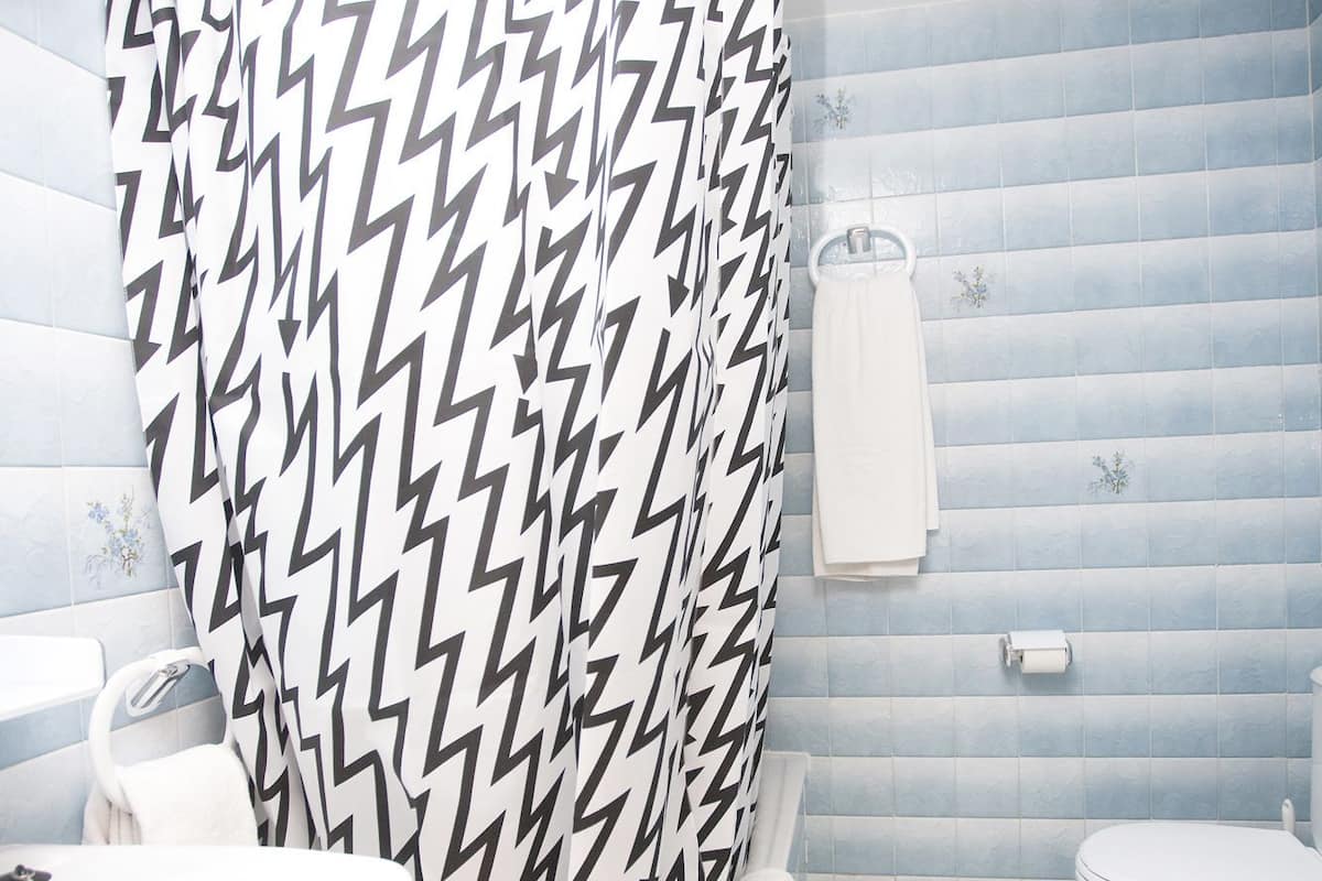 Un baño con cortina de ducha de estampado en zigzag, un inodoro, un lavabo y un perchero para toallas.