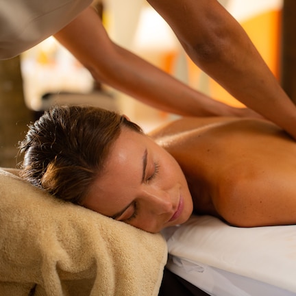 A person receiving a back massage on a bed with a white sheet and a beige blanket.