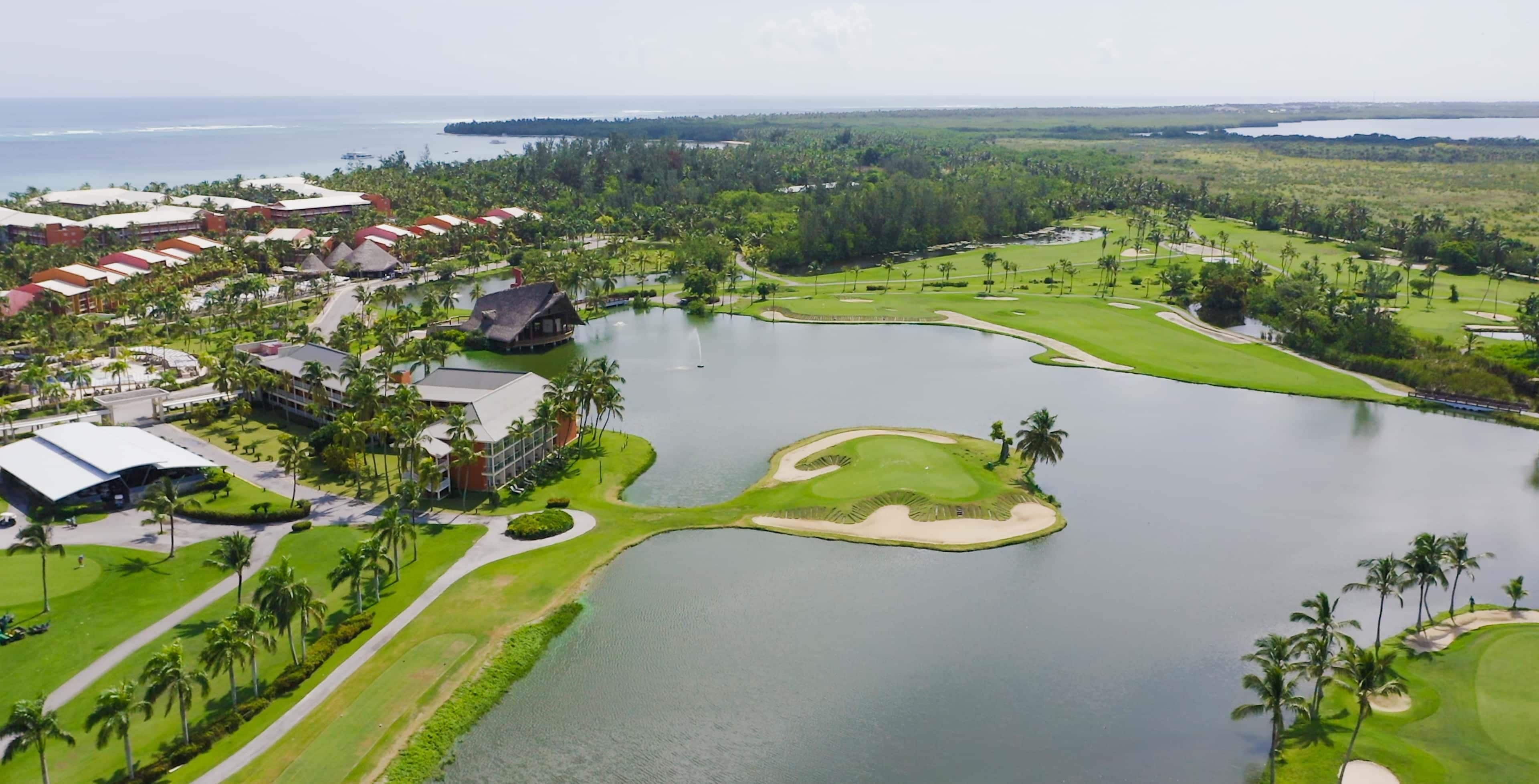 Um campo de golfe com um lago grande, rodeado por vegetação e alguns edifícios.