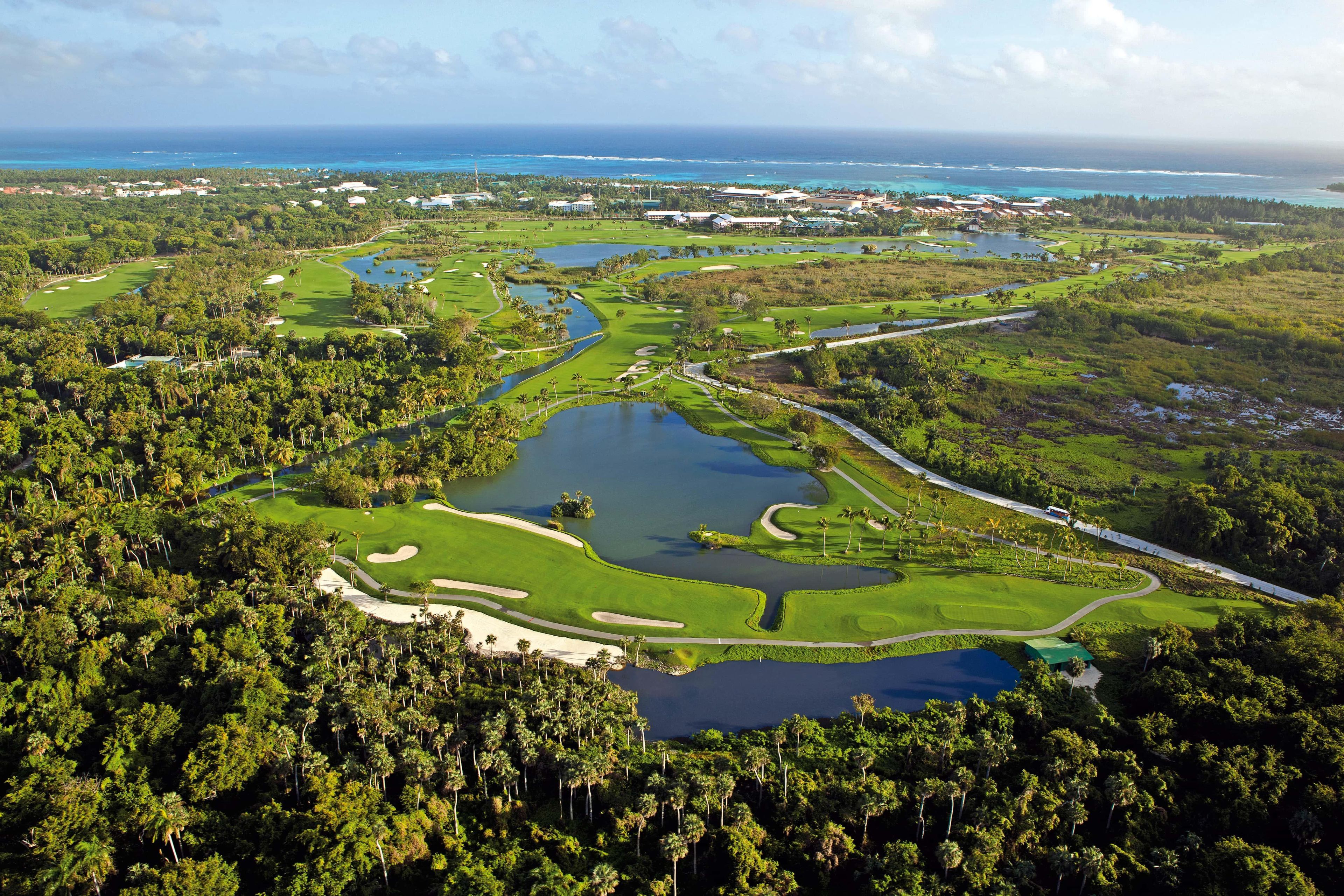 Un parcours de golf comportant de nombreux obstacles d’eau, entouré d’une végétation tropicale luxuriante et offrant une vue dégagée sur l’océan.