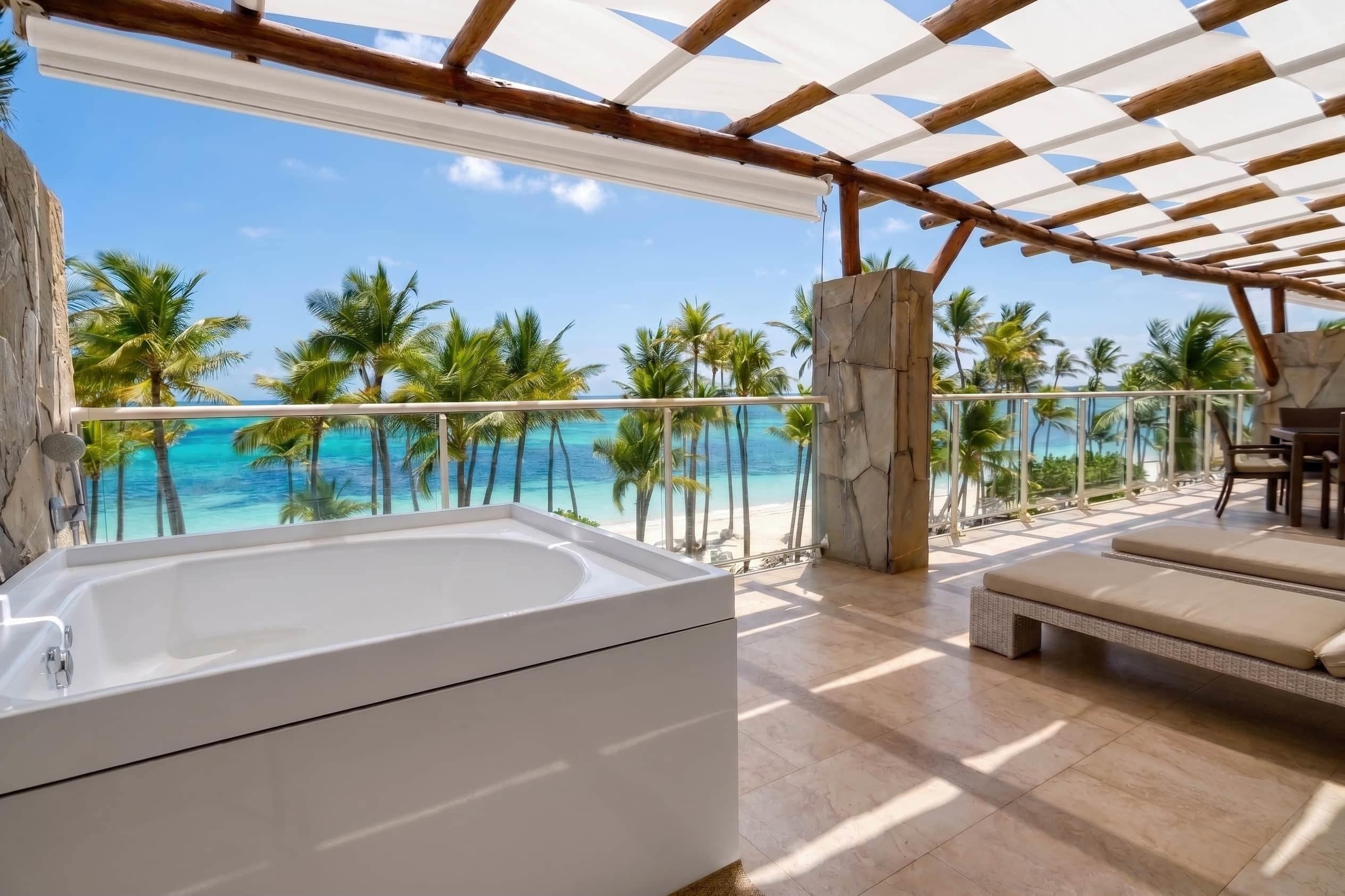 A balcony with a view of the ocean, a jacuzzi, and a seating area.