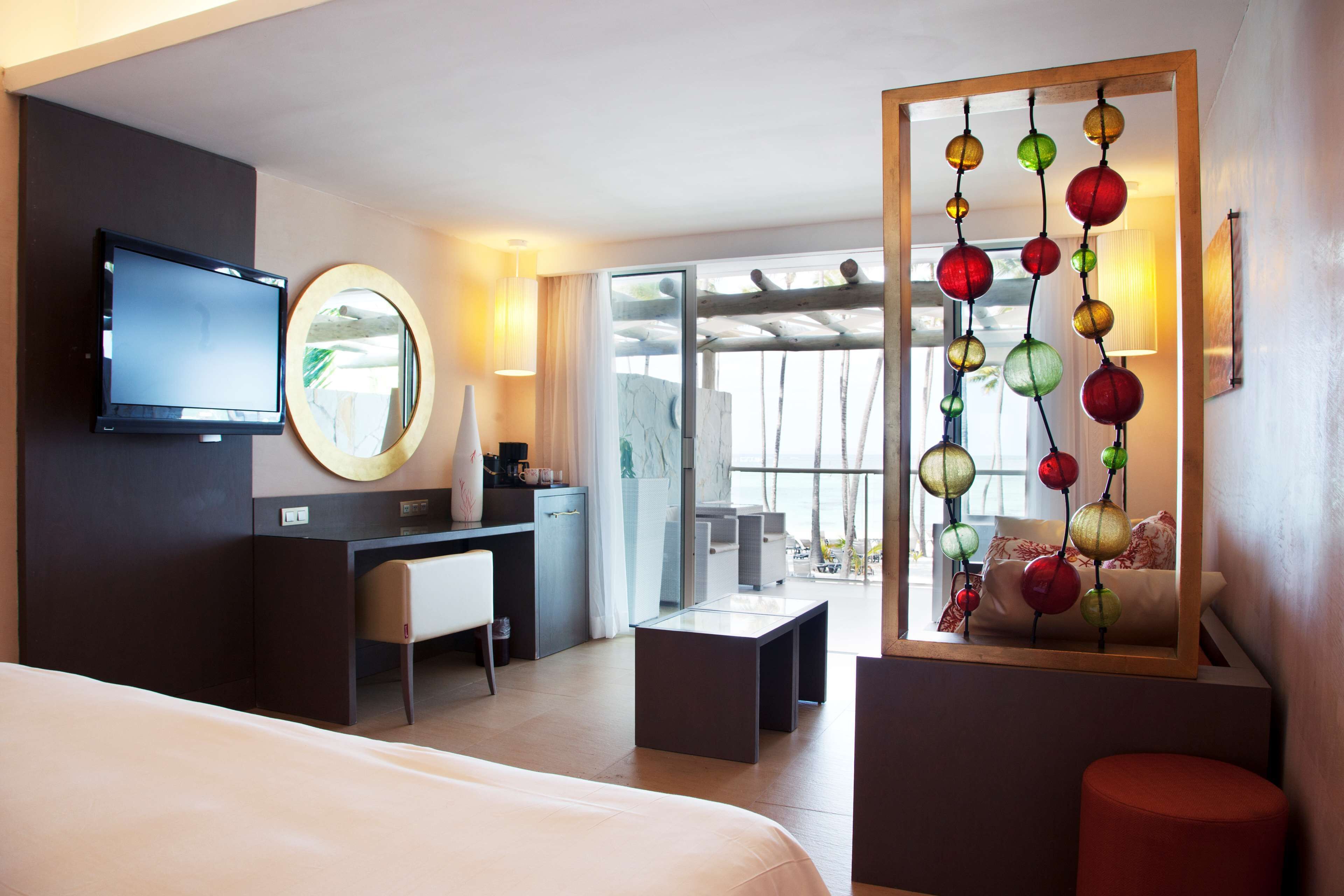 A hotel room with a bed, a desk, a chair, a TV, a mirror, and a balcony with a view.