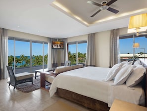 A hotel room with a large bed, a desk, a chair, a TV, and a view of the ocean.