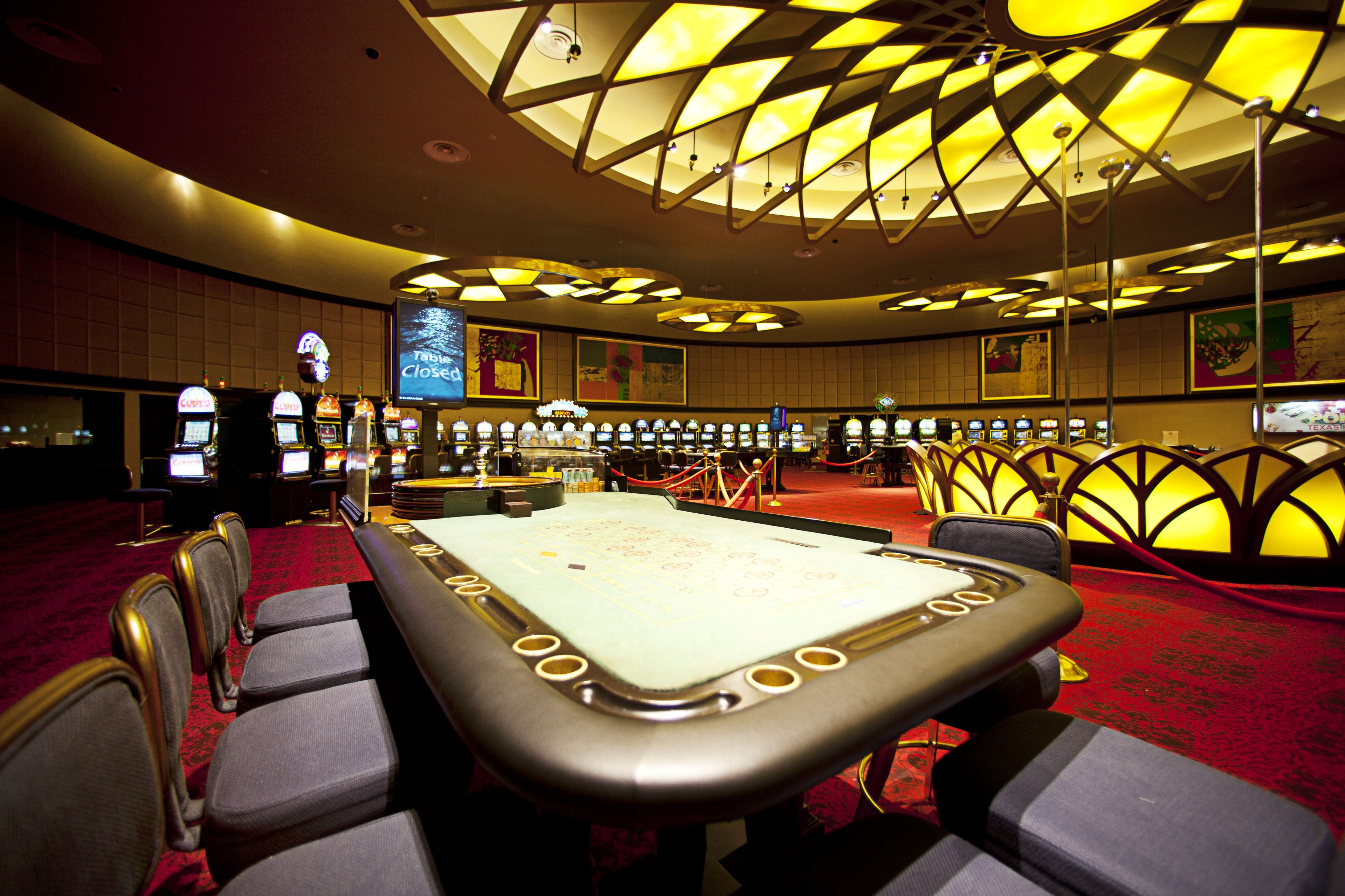 Une salle de casino avec de nombreux appareils à sous, une table de billard et un grand écran indiquant « Table fermée ».