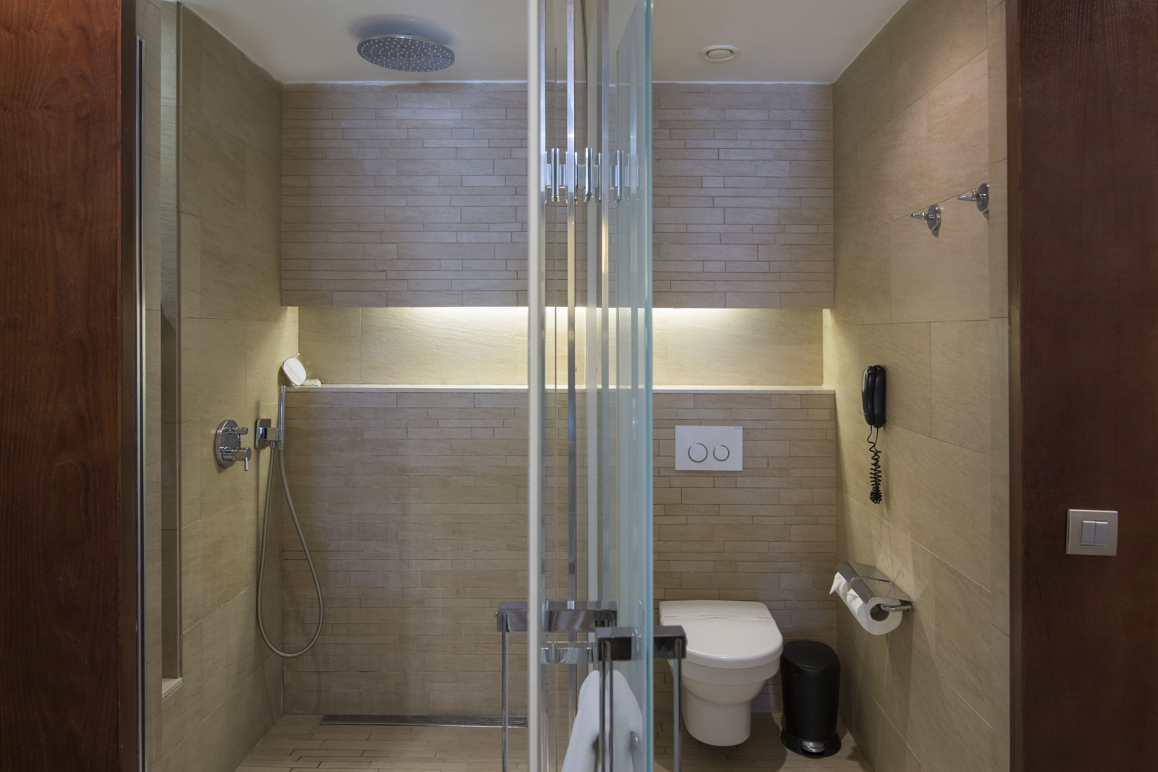 A modern bathroom with a glass-enclosed shower, a toilet, and a trash bin.