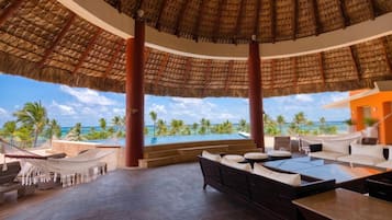 Habitación de resort con vista a la piscina, mobiliario exterior y techo de paja.