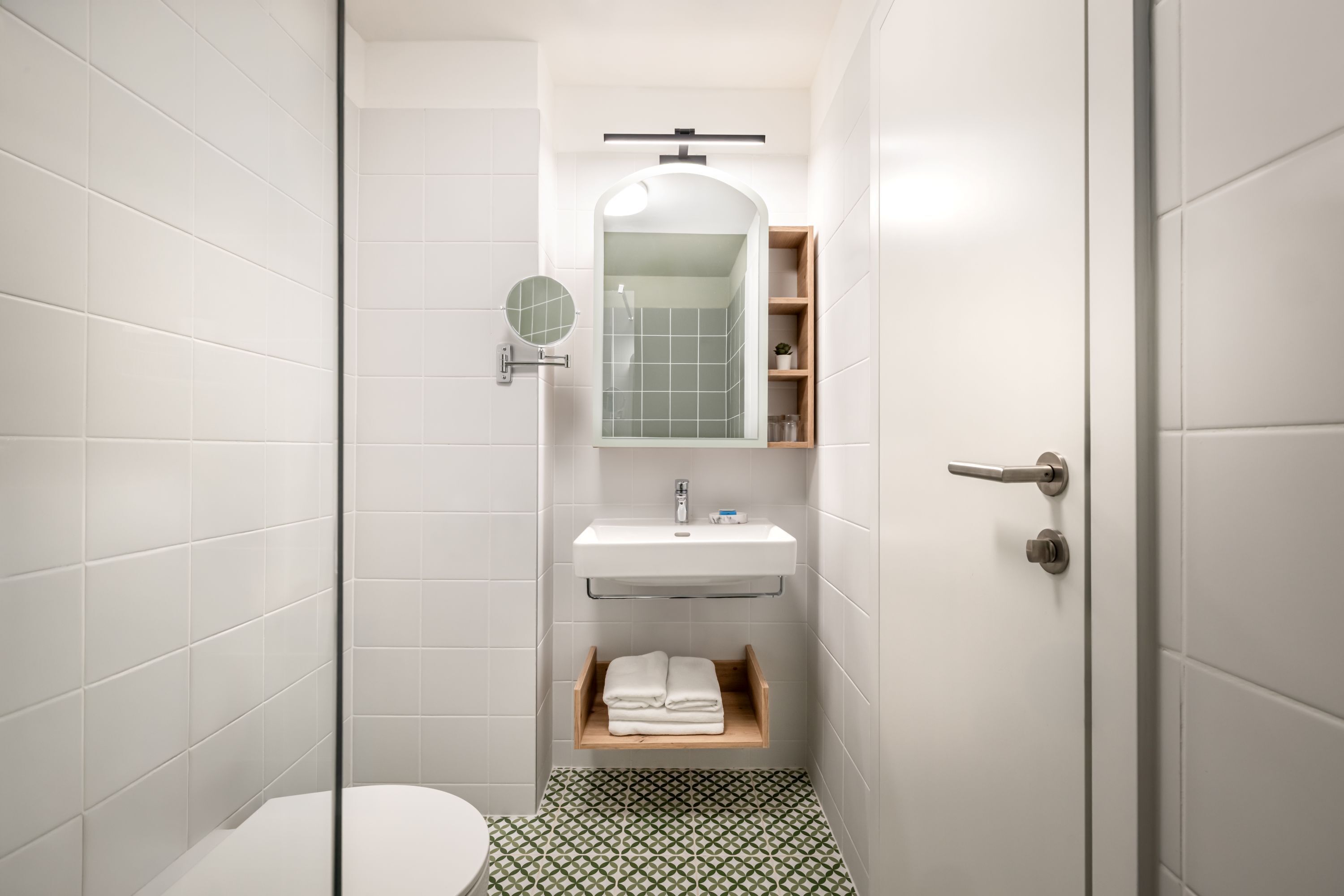A modern bathroom with white tiles, a round mirror, a sink, and a toilet.