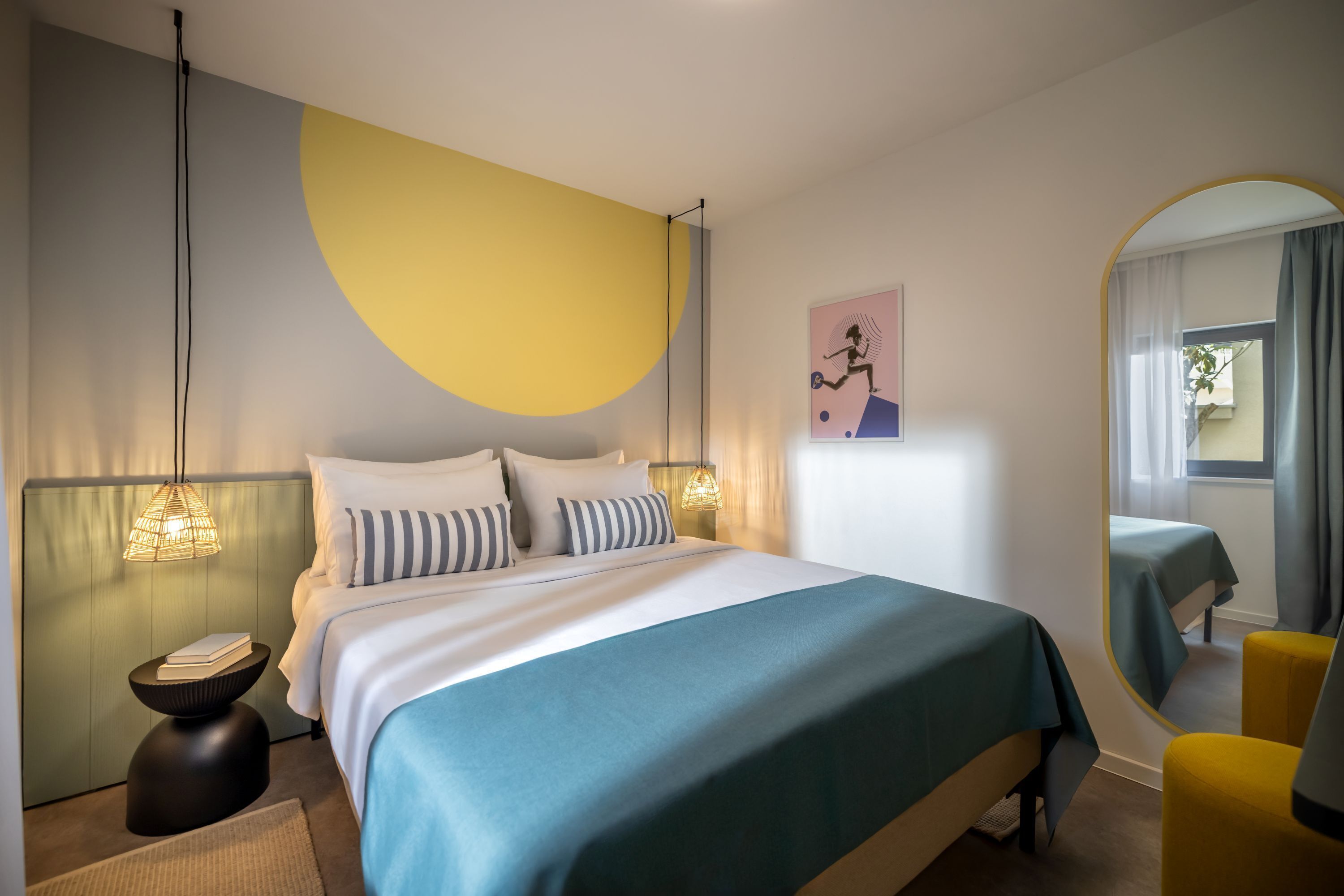 A modern bedroom with a bed, bedside lamps, a bedside table, a mirror, and a window with curtains.