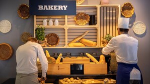 Ett skyltfönster från ett bageri med bröd och bakverk, en skylt med texten ”BAKERI” och dekorativa, flätade korgar.