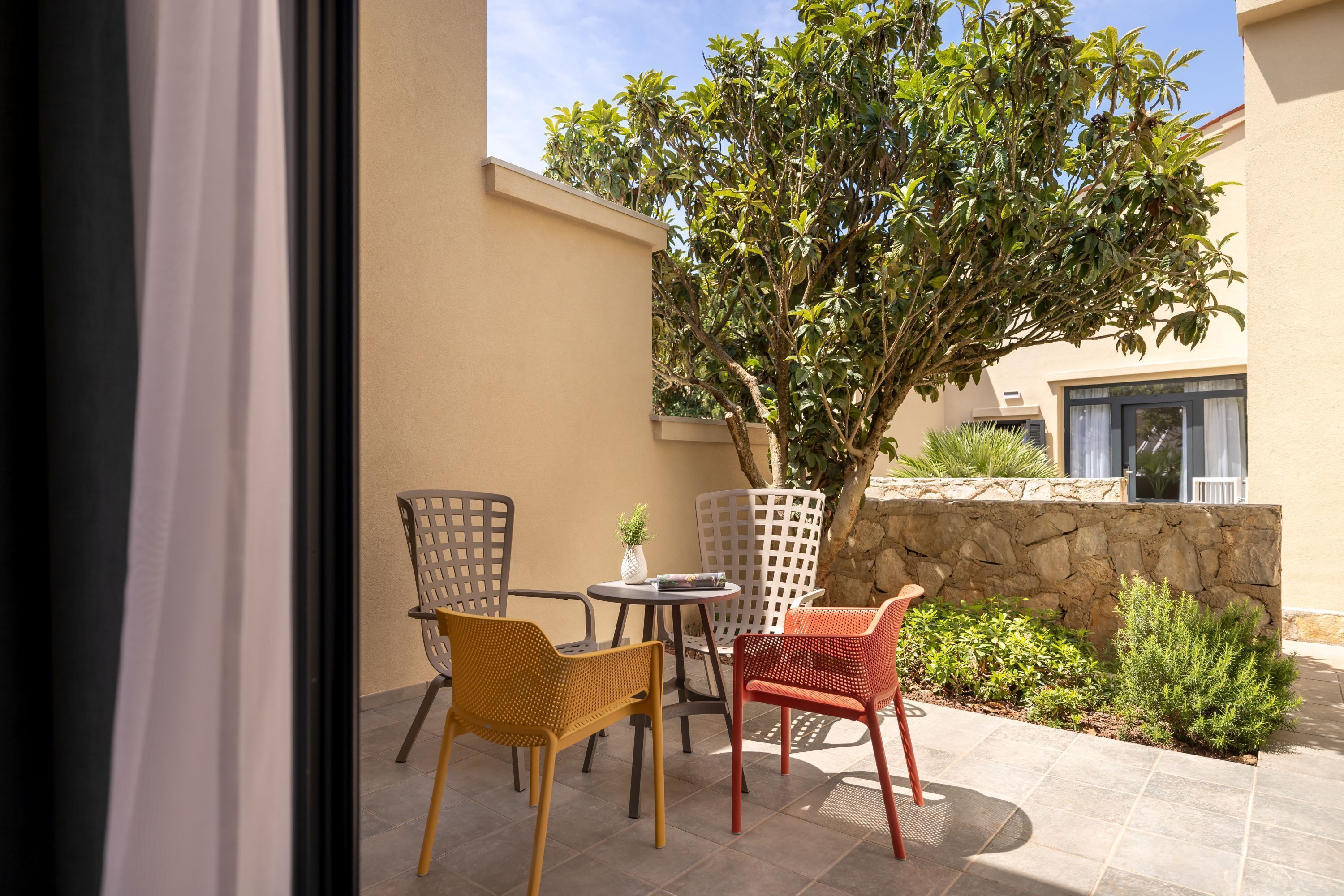 Un patio exterior con dos sillas de mimbre, una mesita redonda y una planta en maceta.