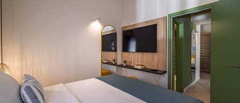 A bedroom with a bed, a desk, a mirror, and a television.