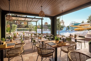 An outdoor dining area with wicker chairs and tables, overlooking a pool and water slides. - Sunny Poreč by Valamar (Porec)