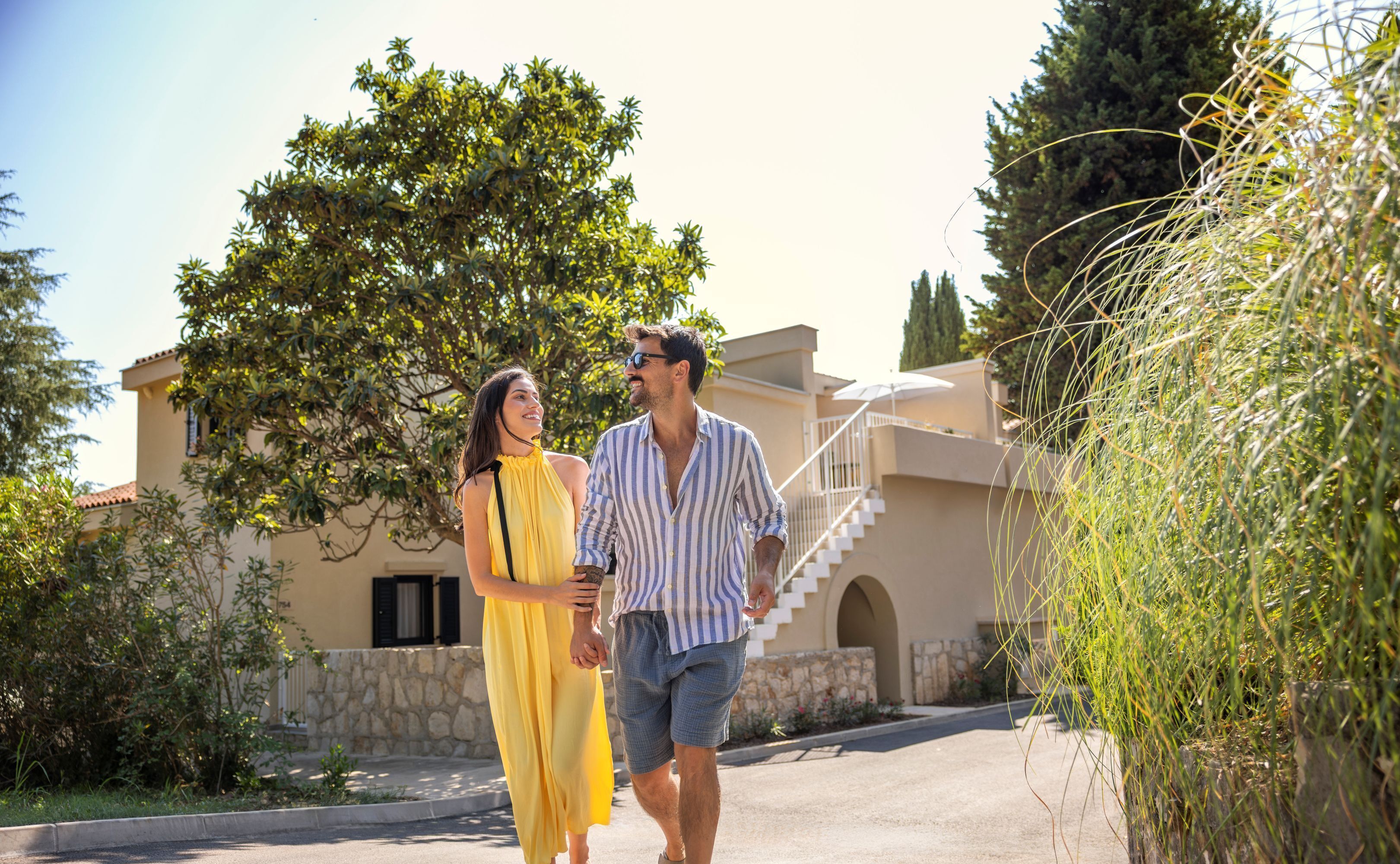 Um casal caminhando por um caminho pavimentado, com um edifício de fachada de pedra e uma escadaria ao fundo.
