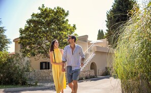 A couple walking on a paved path with a building featuring a stone facade and a staircase in the background. - Sunny Poreč by Valamar (Porec)