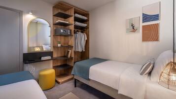 A bedroom with two beds, a wardrobe, a mirror, and artwork on the wall.