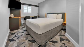 A hotel room with a large bed, a desk, a chair, a flat-screen TV, and a window with blinds.