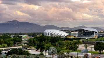 A stadium with a unique, modern architectural design, surrounded by lush greenery and mountains in the background.