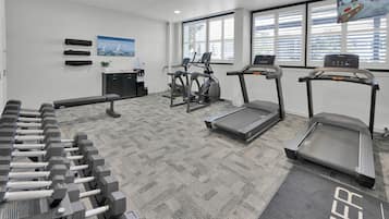 Une salle de sport équipée de tapis de course, de vélos elliptiques et d’haltères.