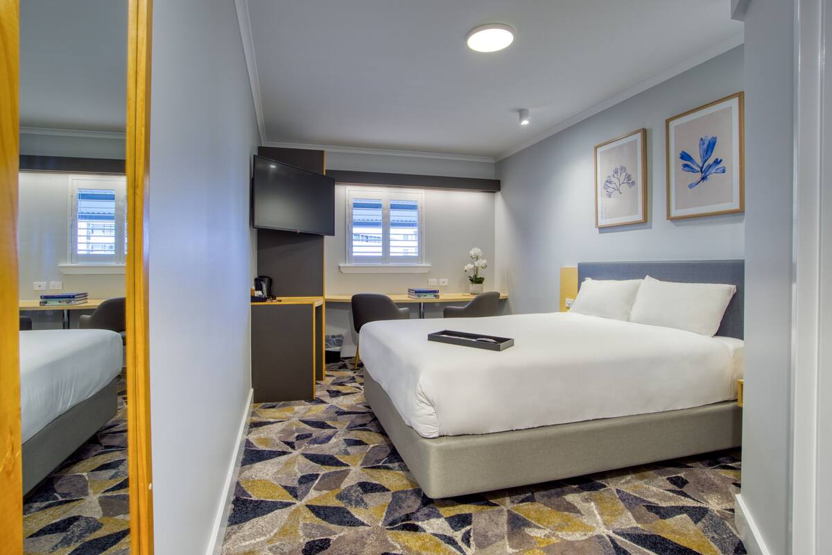 A hotel room with a bed, desk, chair, and a small table with a plant.