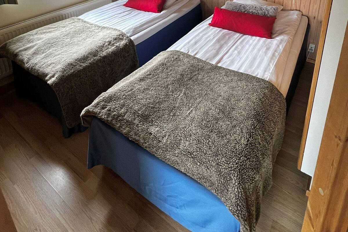 Une chambre avec deux lits, des têtes de lit en bois, une fenêtre avec des rideaux, un tableau encadré au mur et une lampe de chaque côté des lits.