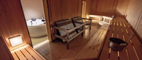 A wooden sauna room with a bench, a table, and a bathtub.