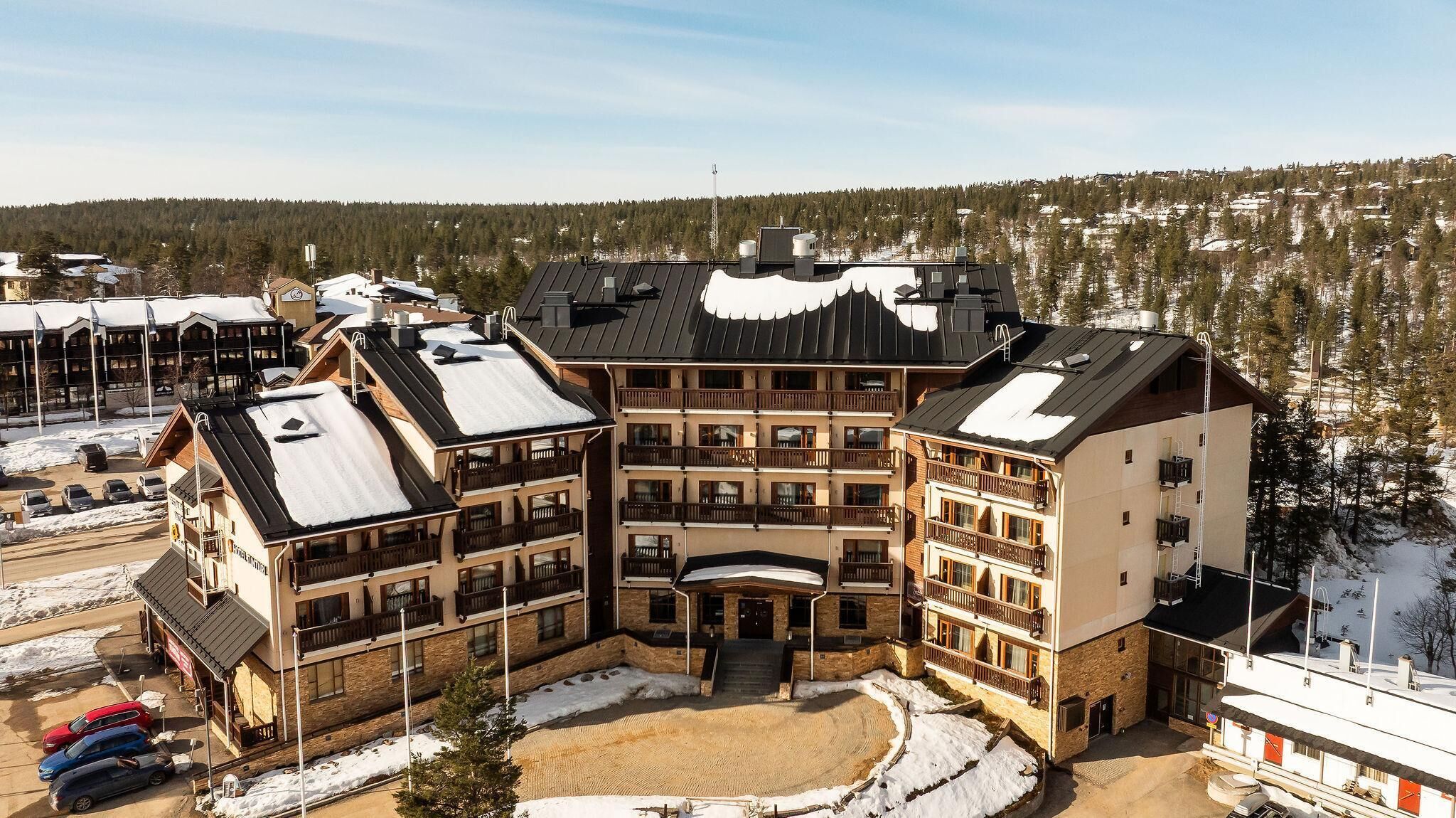 A multi-story hotel with a central courtyard, balconies, and a ski resort backdrop.