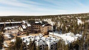 Une station de ski comprenant plusieurs bâtiments, dont un grand chalet doté de balcons, un parking et des toits couverts de neige.