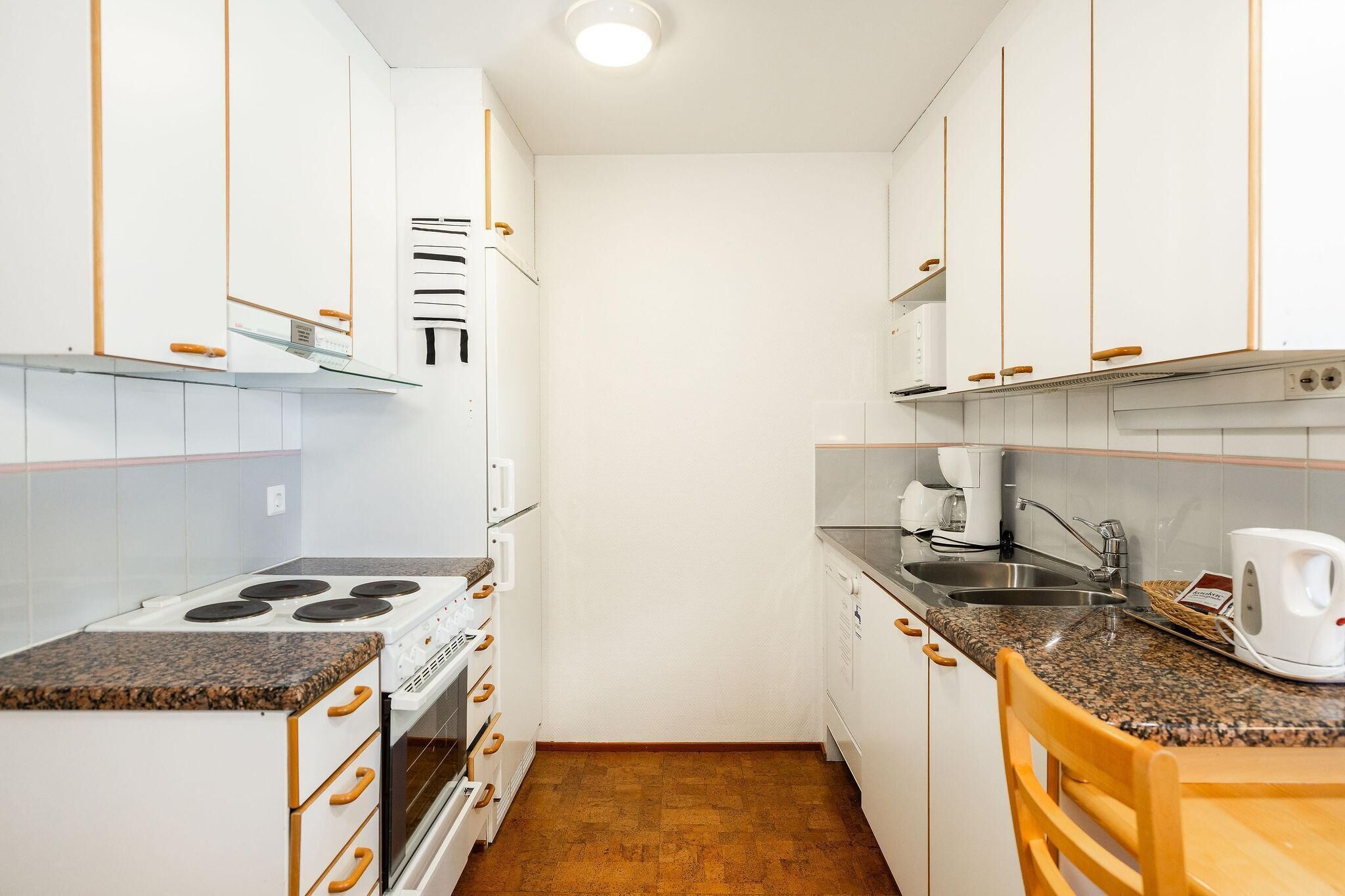 Una cucina compatta con mobili bianchi, un fornello, un lavandino e una macchina per il caffè.
