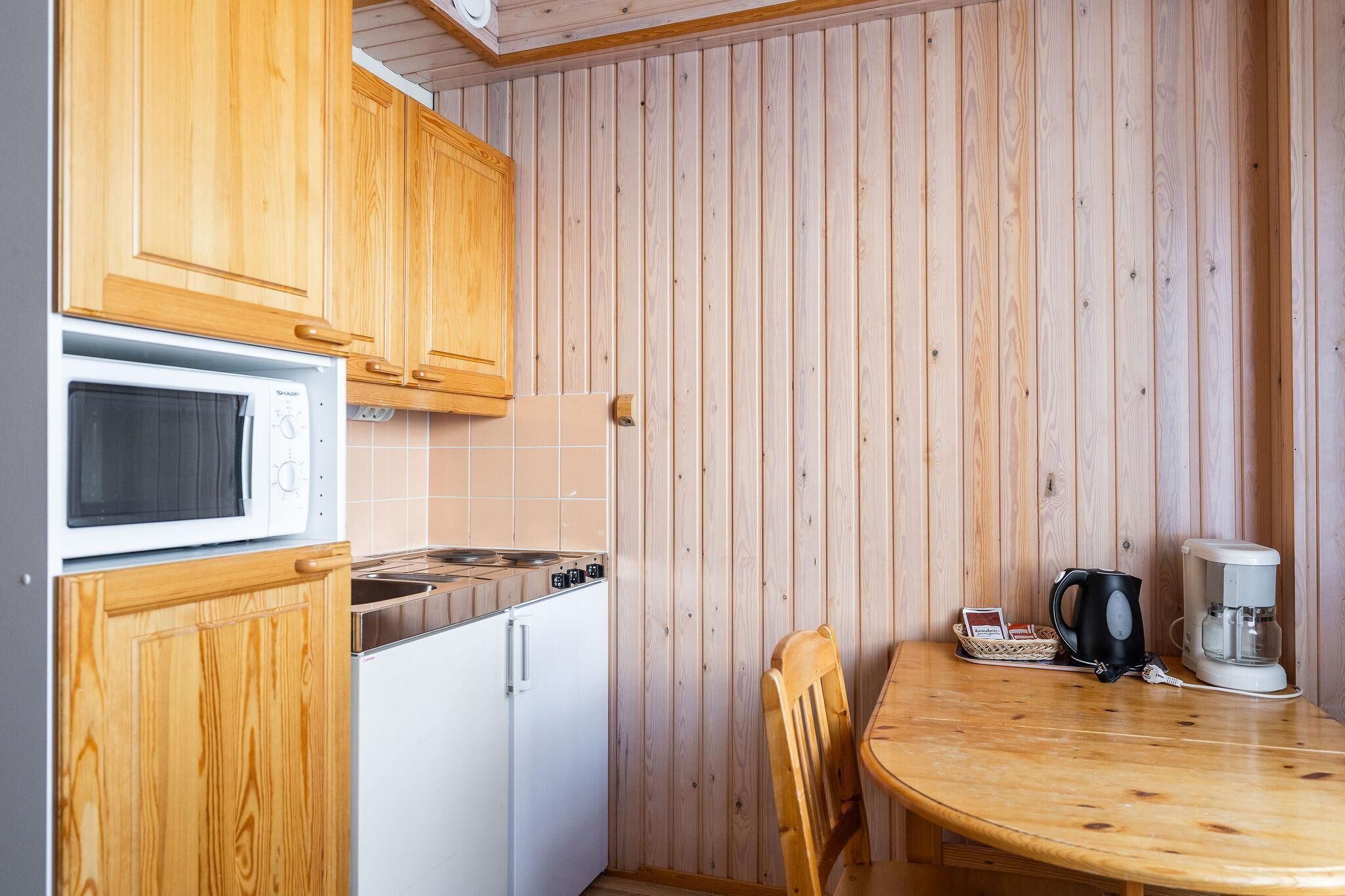 A compact kitchen with wooden cabinets, a microwave, a stove, and a coffee maker on a wooden table.
