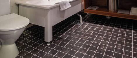 Un baño moderno con techo de madera, ducha con cerramiento de vidrio, bañera blanca y piso de baldosas negras.