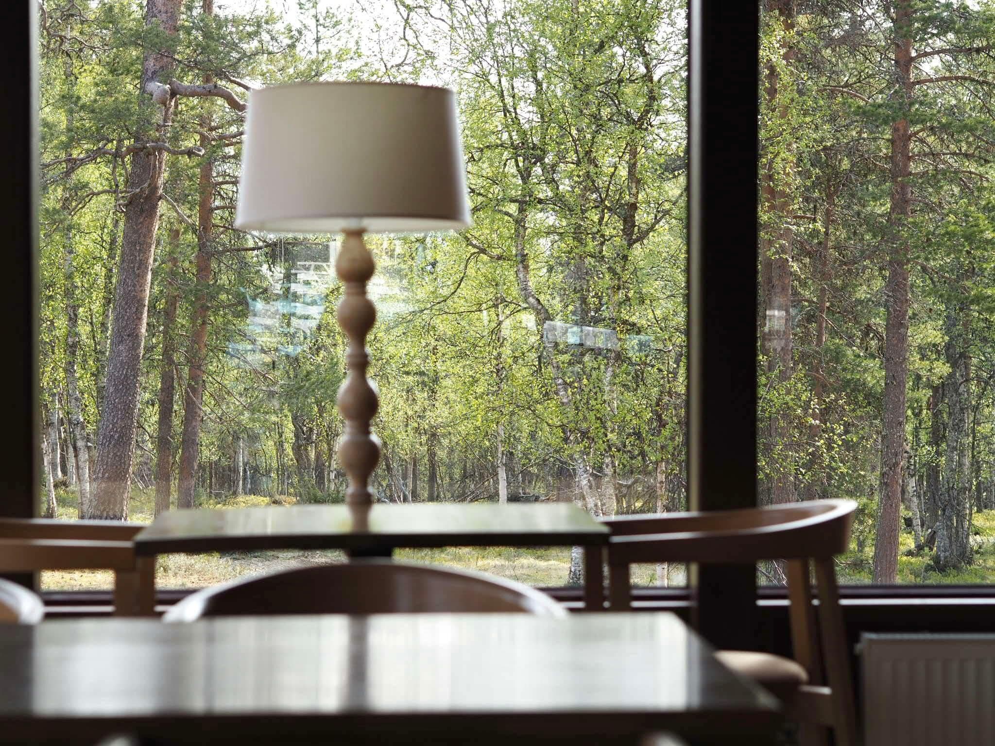 Una mesa con una lámpara en una habitación con vistas a un bosque.