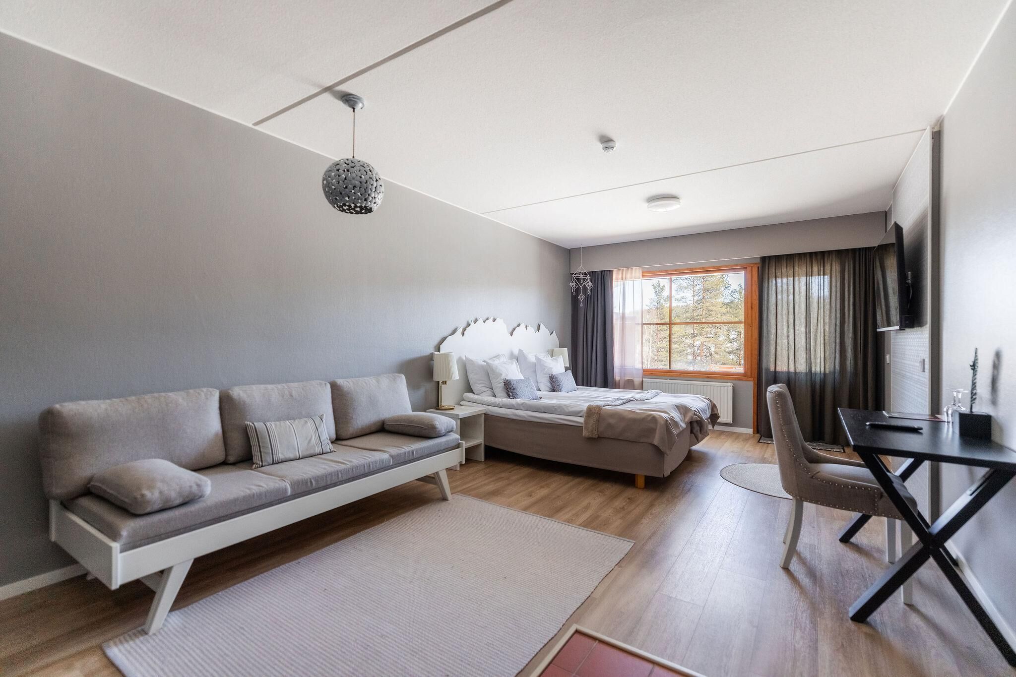 A modern bedroom with a sofa, bed, desk, and a TV.
