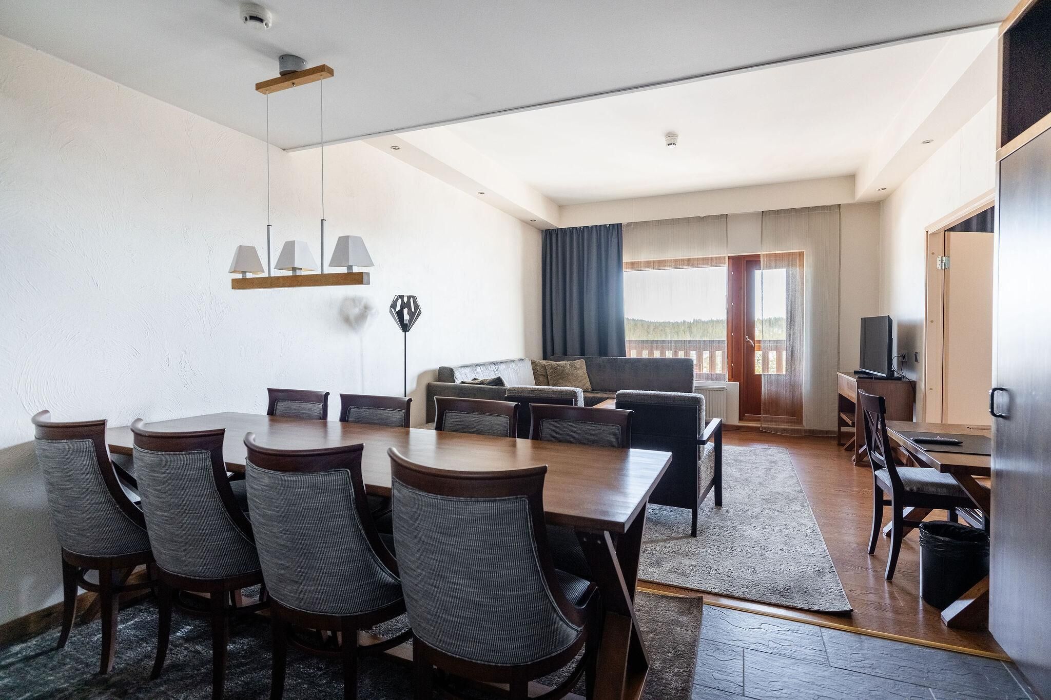Habitación de hotel con comedor, un sofá, televisor y un ventanal grande.