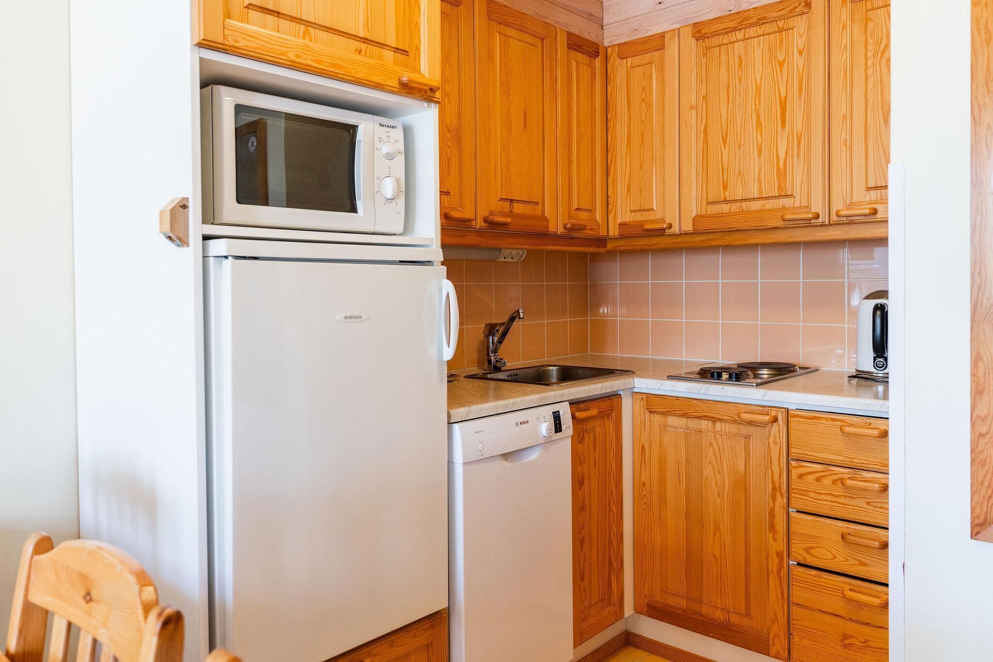 A compact kitchen with wooden cabinets, a microwave, a dishwasher, and a sink.
