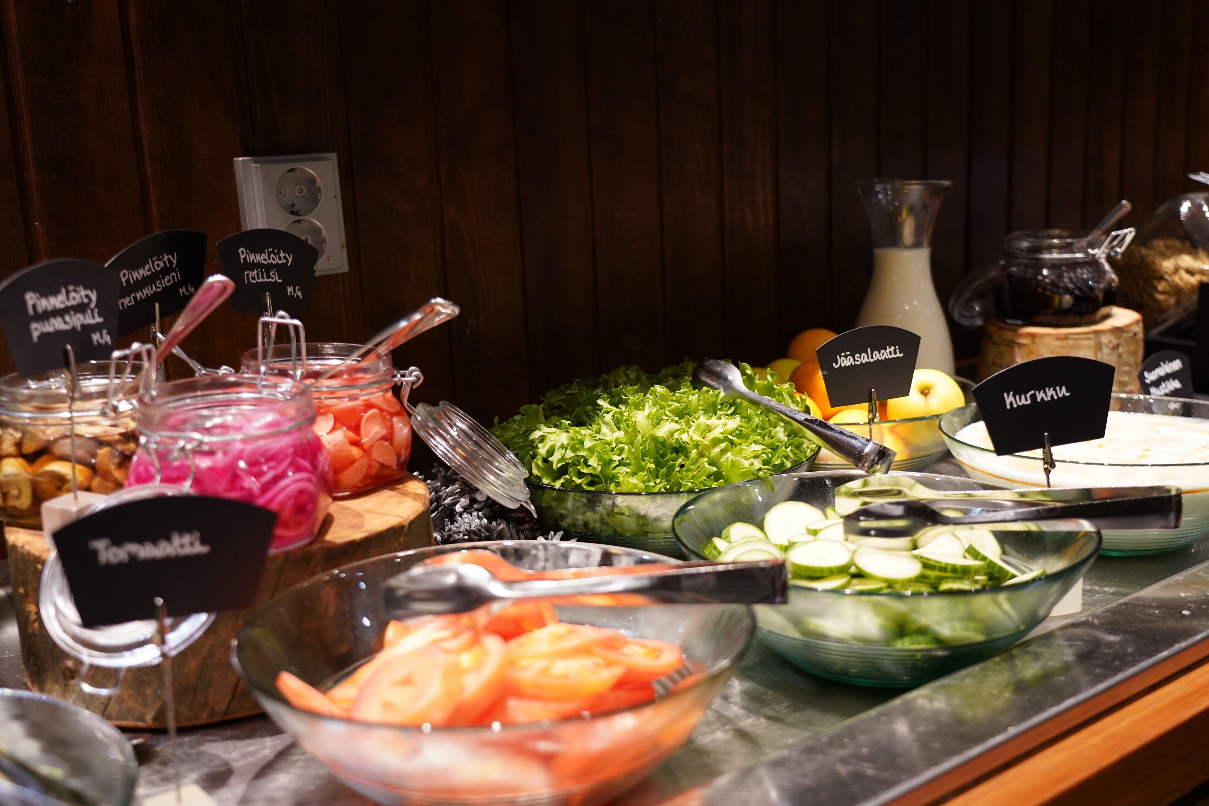 Un bufé con diversos alimentos, incluyendo tomates, pepinos y una ensalada.