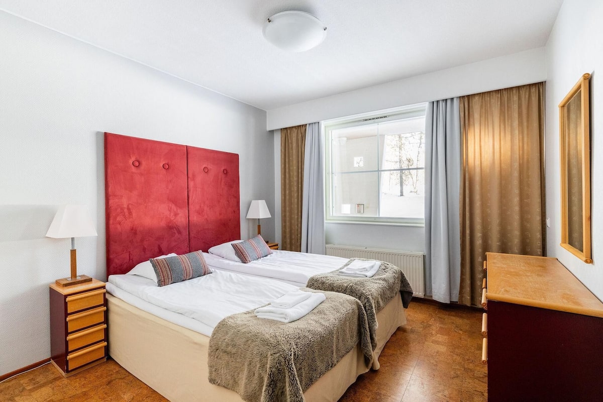 Une chambre d’hôtel avec un lit double, une petite table de chevet, une lampe, une fenêtre avec des rideaux et une commode en bois.