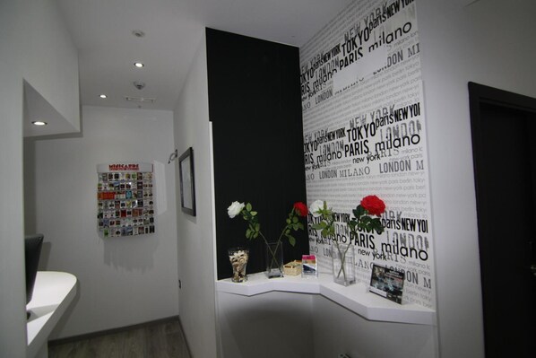 A reception area with a wall display of city names, a framed photo, and a small table with a vase and a book. - Hostal MH Fuencarral (Madrid)